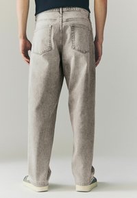 Lichtgrijze denim jeans met een losse pasvorm, met twee achterzakken en zichtbare stiksels. Gecombineerd met casual sneakers.