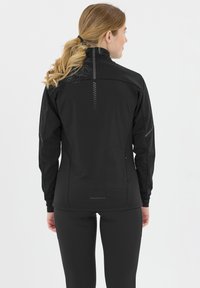 Svart idrottsjacka med hög krage, med subtila reflekterande detaljer och en ficka med dragkedja på baksidan. Sittande design.