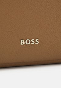 Brązowy portfel skórzany o fakturze z złotym logo "BOSS" umieszczonym na dole na środku, co stanowi element identyfikacji marki. Prosty i elegancki design.