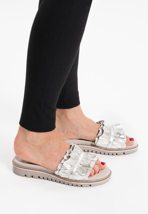 Voeten met zilveren slides met gerimpelde bandjes en rode teennagellak, gecombineerd met zwarte strakke broek.