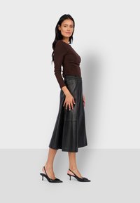 Top marrone a maniche lunghe con arricciature, abbinato a una gonna midi in pelle nera. Il look è completato da scarpe slingback nere con punta affusolata.