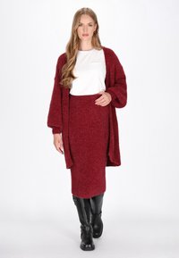 Bordeaux stickad cardigan med oversized ärmar, kombinerad med en matchande kroppsnära kjol. Modellen har på sig svarta knähöga stövlar. Vit topp under.