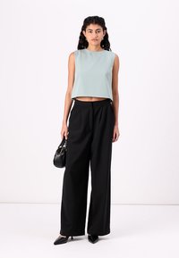 Světle zelený bezrukávový crop top, černé široké kalhoty, malá černá kabelka, špičaté černé boty. Hladký materiál, minimalistický design.