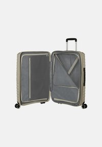 Valigia rigida beige con manico telescopico, interno grigio, tasche con zip e un esterno testurizzato con linee orizzontali.