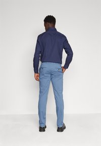 Camicia abbottonata blu navy con maniche lunghe, abbinata a pantaloni blu chiaro. I pantaloni sono dotati di tasche posteriori con chiusura a bottone.