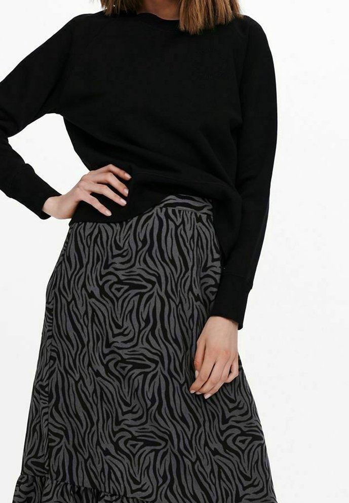 Top de manga larga negra acompañado de una falda gris con estampado de cebra y un dobladillo con volantes. La tela parece suave y texturizada.