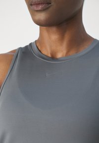 Gros plan d’une personne portant un haut de sport gris sans manches avec un logo Nike discret sur la poitrine.