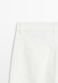 Vue arrière d'un pantalon en denim blanc montrant des passants de ceinture et une poche arrière avec des coutures visibles.