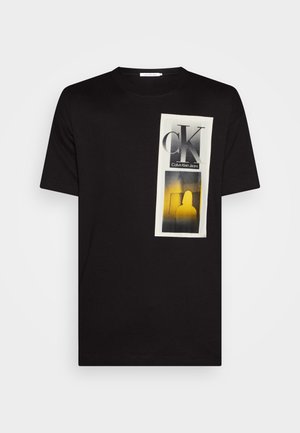 Zwarte katoenen t-shirt met een grafische print aan de voorkant in wit, grijs en geel. Het ontwerp bevat een "CK"-logo en silhouet binnen een rechthoekige accent.