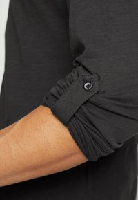 Zwart langemouwen shirt met een gather cuff, voorzien van een knoopdetail, gemaakt van een textiel met een subtiele glans.