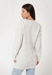 Crème oversized trui met een textuur gebreid patroon, geribde manchetten en zoom. Van achteren getoond, gecombineerd met lichtblauwe jeans.