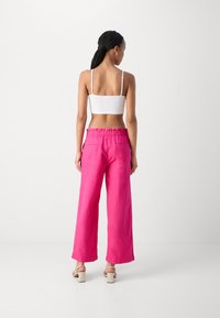Rosa vide benbukser med elastisk talje og to baklommer, sammen med en hvit spaghetti-stropp topp og nøytrale block-heeled sandaler.