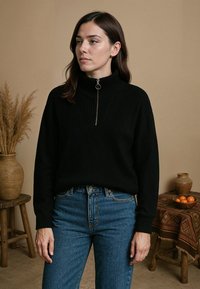 Zwarte gebreide trui met hoge kraag en ritssluiting, met ribbeltextuur. Gecombineerd met blauwe high-waisted jeans. Neutrale achtergrond.