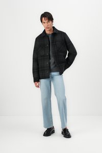 Svart og grå rutete jakke med to brystlommer, brukt over en mørk genser, kombinert med lyseblå jeans og svarte sko.