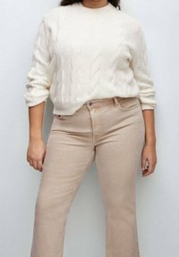 Kermavajoneule, jossa on pitkät hihat, yhdistettynä vaaleanbeigeihin vaaleisiin farkkuihin. Neuleessa on rakenteellinen kuvio; farkuissa on klassinen viiden taskun malli.