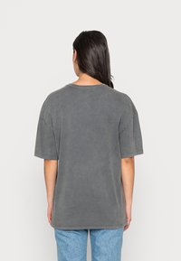 Camiseta gris de gran tamaño con mangas cortas y cuello redondo. Tejido suave y texturizado con un corte holgado, que presenta detalles de costuras visibles.