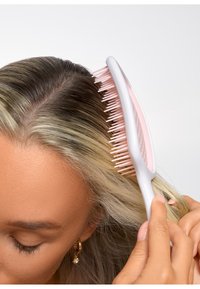Uppsättningskamm med vitt handtag och rosa borst, utformad för enkel hantering av hår. Har breda tänder för lätt användning.