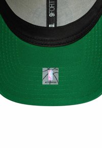 Grüne Baseballmütze mit einem schwarzen Schirm, flachem Rand und NBA-Logo-Aufkleber auf der Innenseite. Der Stoff hat eine glatte Textur und genähte Akzente.