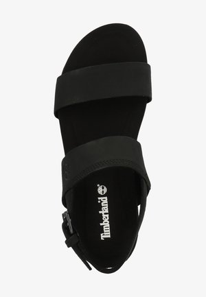 Sandalía negra con correas anchas, suela plana y hebilla ajustable. Textura suave con logo impreso en la plantilla. Diseño sencillo y abierto.