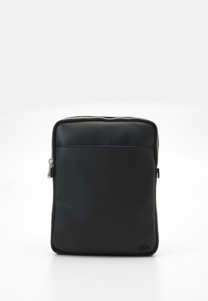 Pochette rectangulaire en cuir noir avec une poche frontale, une fermeture éclair sur le dessus et un logo discret en relief dans le coin inférieur.