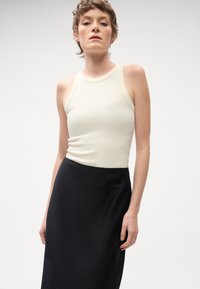 Kremowy, bezrękawnikowy top o prążkowanej fakturze, w połączeniu z czarną, gładką spódnicą o dopasowanym kroju i wysokim dekolcie, bez widocznych wzorów czy akcentów.