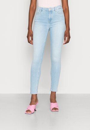 Vaqueros ajustados de un azul claro, confeccionados en denim, con una cintura alta y un ligero desgastado. Combinados con zuecos rosas con tiras cruzadas y un tacón cuadrado.