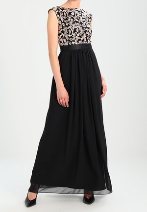 Femme portant une robe de soirée noire sans manches avec un corsage argenté et noir à motif et des escarpins noirs à bout pointu.