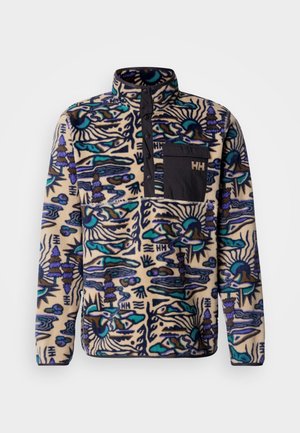 Vilnos megztinis su aukštu kaklu, mėlyna, juoda ir violetine raštais ant kreminio fono; turi kišenę krūtinės srityje su logotipu.