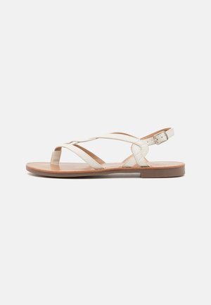 White leather sandals with cross-strap design, open toe, and adjustable ankle buckle. Flat sole in brown with smooth texture.