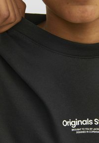 Camiseta de algodón negra con cuello acanalado. Presenta texto impreso en blanco en la parte frontal. Vista en primer plano que muestra la textura suave de la tela.