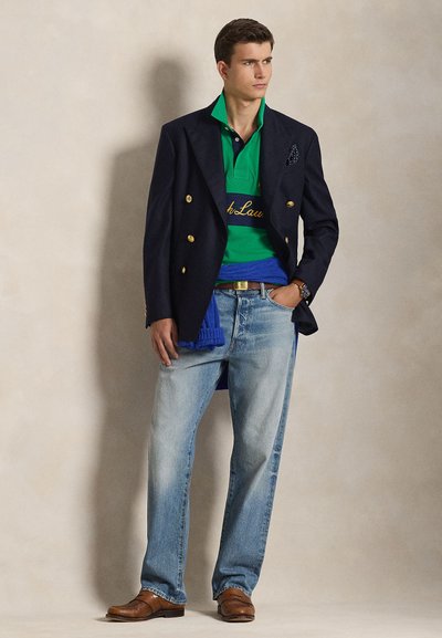 Μπλε διπλόξαντρο σακάκι, πράσινο πόλο με μπλε ρίγες, ανοιχτόχρωμα μπλε τζιν, καφέ παπούτσια. Διακριτικά χρυσά κουμπιά και λεπτομέρεια με μαντιλάκι στην τσέπη.