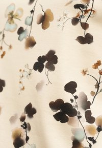 Tissu crème doux avec un motif délicat de groupes floraux abstraits dans des tons de brun, beige, noir et bleu clair.