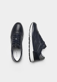 Baskets en cuir bleu marine avec une finition texturée, présentant un design à lacets, une semelle blanche et de subtils accents perforés sur les côtés.