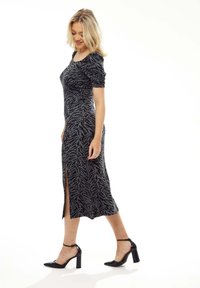 Black and grey zebra-patterned dress with short ruched sleeves and a side slit, paired with black heeled shoes. Smooth fabric texture.