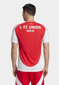 Maillot de sport rouge et blanc avec "1. FC UNION BERLIN" imprimé au dos. Conçu avec des manches courtes et une texture en maille pour la respirabilité.