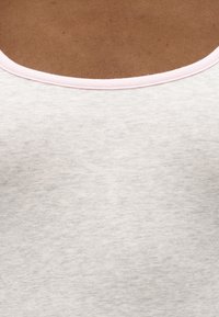 Κοντινή λήψη του λαιμού και του άνω μέρους του στήθους ενός ατόμου που φορά ένα ανοιχτό γκρι πουκάμισο με ανοικτό ροζ στρογγυλή λαιμόκοψη.