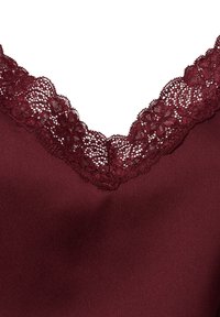 Burgundowa bezrękawnik z teksturowanym koronkowym dekoltem w kształcie litery V i gładkim materiałem, ozdobiony skomplikowanym koronkowym detalem w kwiaty wzdłuż krawędzi.