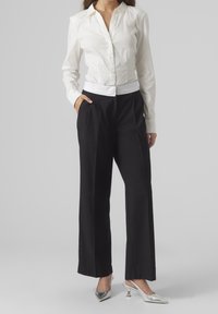 Camicia bianca con bottoni, dal taglio aderente e maniche lunghe, abbinata a pantaloni neri a gamba larga con un cinturino decorato in bianco. Tacchi argento.