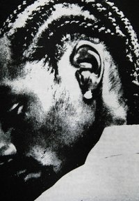 Foto ravvicinata in bianco e nero della testa di un uomo girata di lato, che mostra capelli intrecciati, orecchio con orecchino e parte di un colletto.