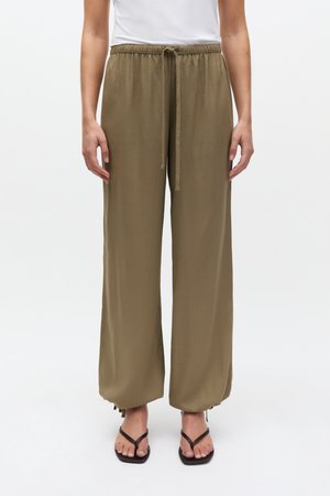 Pantalon large couleur olive avec taille élastique et cordon de serrage. Confectionné dans un tissu doux, il présente des ourlets ouverts pour une coupe décontractée.