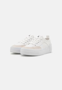 Sneakers bianchi in tela con punta in suede beige, suole spesse bianche stratificate e design con lacci. Include un tallone per il tiraggio.