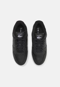 Sneakers in pelle nera con finitura testurizzata, dotati di una suola in gomma bianca, lacci rotondi e il logo Lacoste sulla linguetta e sul lato.