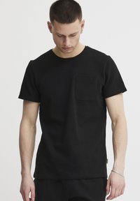 Sort kortærmet t-shirt med rund halsudskæring og en brystlomme. Stoffet har en struktureret overflade. Ingen synlige mønstre eller grafik.