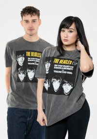 Gray cotton t-shirts featuring The Beatles graphic print, square design with black and white faces, yellow text, and relaxed fit on model.
