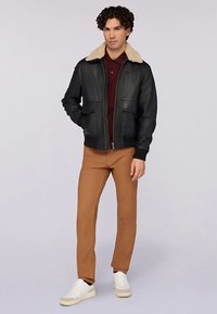 Černá kožená bunda s béžovým kožíškovým límcem, předním zipem a dvěma velkými kapsami. Kombinováno s béžovými kalhotami a bílými teniskami.