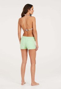 Zelené plavky s elastickým pasem a zadní kapsou; látka vypadá lehká. Top je v halter stylu s mnohobarevným vzorem.