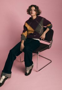 Maglione lavorato a maglia multicolore con motivi a diamante in bordeaux, senape, grigio e bianco. Abbinato a jeans scuri e sneakers marroni.