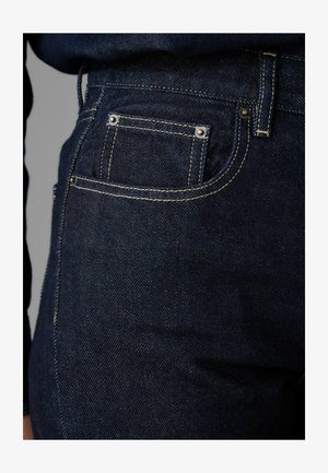 Tmavě modré džíny s klasickým pětipocketovým designem, kontrastním prošíváním a kovovými nýty. Textura se zdá hladká s mírným leskem.