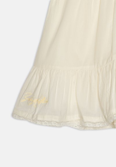Robe en coton couleur crème avec un ourlet volanté, une délicate bordure en dentelle et un texte brodé en or près du bas.