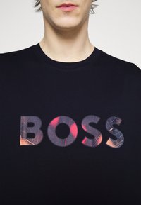 Svart bomullströja med rund halsringning som har en stor, texturerad "BOSS"-logotyp i flerfärgad tryck.